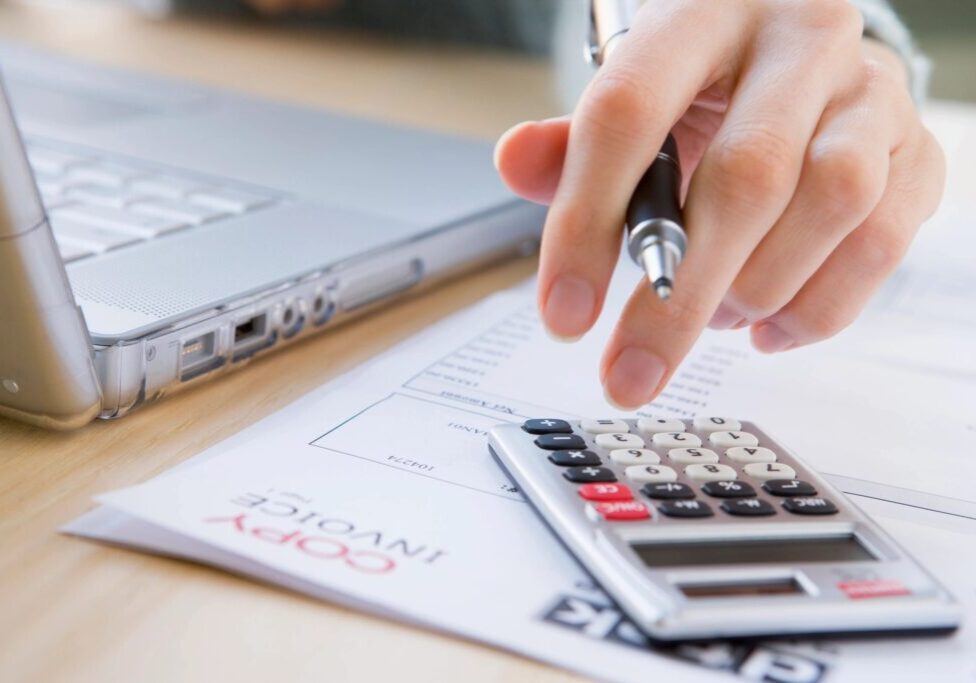 Person calculating finances using a calculator and laptop.