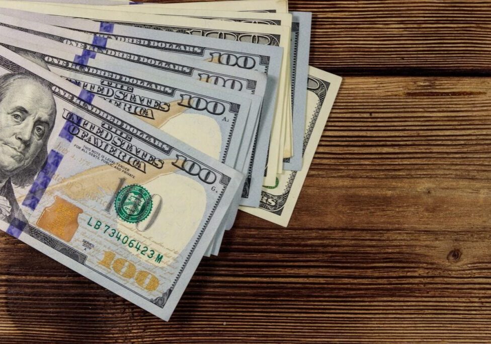 Stacks of US $100 bills on a wooden surface.