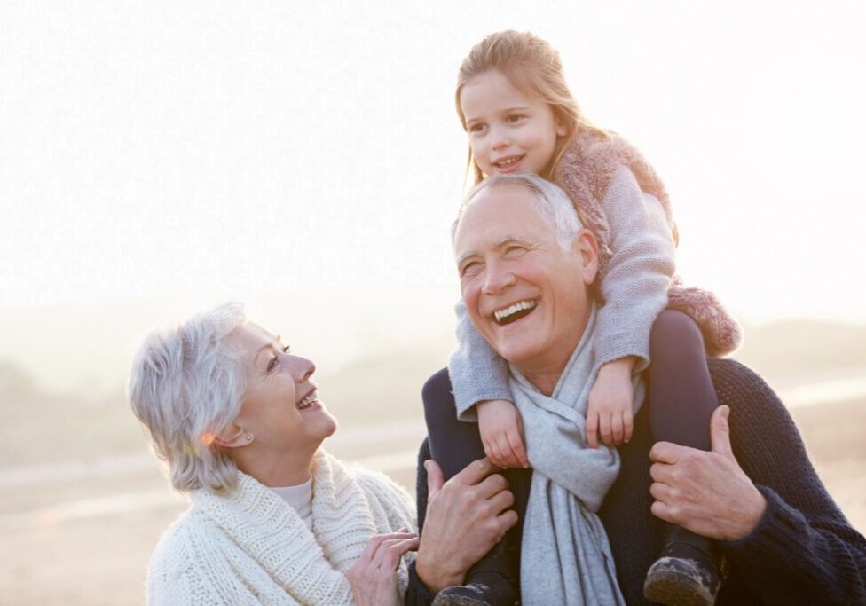 Happy elderly couple with granddaughter outdoors, sharing joyful moments.