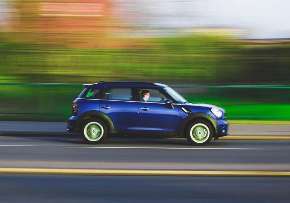 Blue Mini Cooper driving fast on a city street.